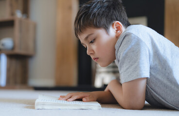 Portrait School kid reading a book for homework, Young boy lying on carpet enjoy reading the story in living room, Child relaxing at home on weekend. Home Schooling or Education concept
