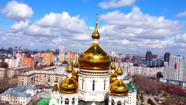 Golden domes of a Christian church. Against the background of a blue cloudy sky and the city. The Russian Far East. Flying around by drone. 