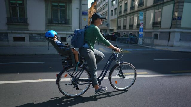 Happy woman riding bicycle with sleeping child in back seat in urban street