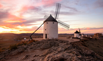Old windmills at sunset in Castilla la Mancha, Spain, touristic place for Cervantes' novel, Don Quixote - obrazy, fototapety, plakaty
