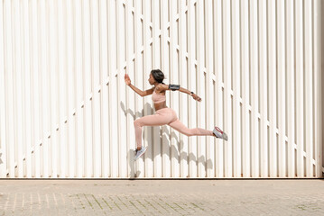 Young African American sporty woman jumping up and running against light background. Female model...