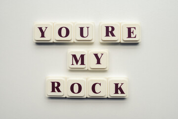 Closeup of scrabble tiles with letters spelling the message "You're my rock" on a white background