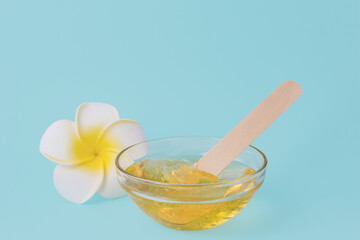 Liquid yellow sugar paste, wooden spatula and flower on a blue background. Removing unwanted hair. Sugaring.Depilation. Epilation. Beauty. Place for text. - obrazy, fototapety, plakaty