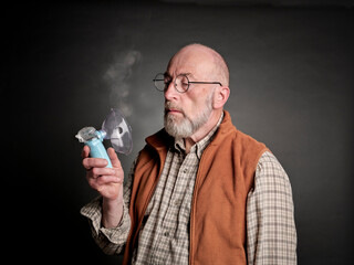 Head and shoulders portrait of a senior man using a portable handheld nebulizer, self care and respiratory therapy concept