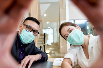 Fototapeta na wymiar Businessman and woman take a selfie by mobile phone and wear the facial mask in office