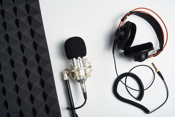 Microphone, headphones and heart shaped cable on on white background with acoustic foam panel on...