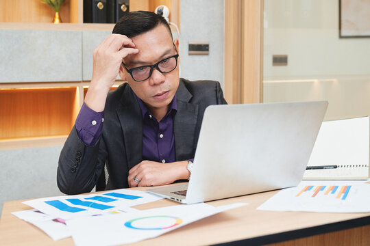 Asian Businessman In Purple Shirt And Black Suit Worry About Work On Laptop In Office