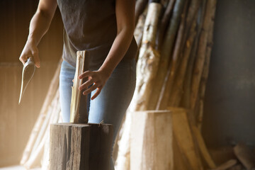 close-up of an unrecognizable woman holding a piece of wood to split it into smaller pieces to make firewood. logs in the background