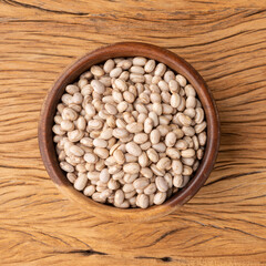 Raw brown beans in a wooden bowl over wooden table
