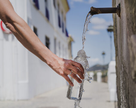 photo of a hand holding a glass bottle filling it with natural water from a fountain