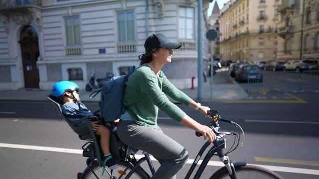 Parent riding bicycle in street with sleeping child in back seat mother rides bike