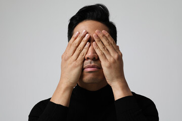 Headshot of Asian young man is covering eyes. Mental health issues. Isolated.