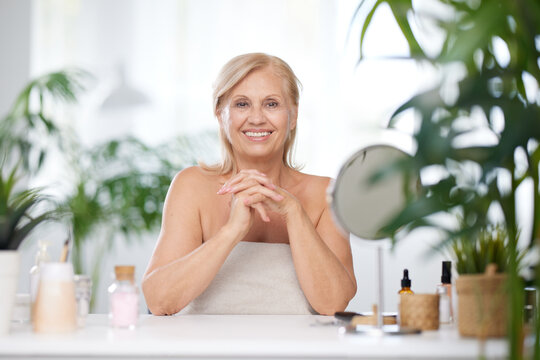 A senior blond woman is sitting at home surrounded by beauty products. Beauty and seniors, makeup for senior woman