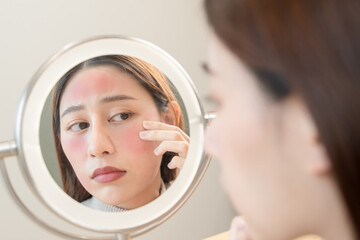 Young Asian woman looking in the mirror worried cosmetics allergy on face skin