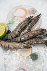 Raw whole fresh uncooked prawns shrimps on decorated ice with lime on gray stone background.