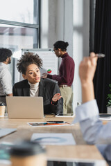 Fototapeta premium African american businesswoman pointing with hand near devices and blurred colleague in office.