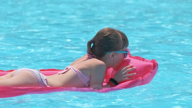 Young joyful child girl having fun swimming on inflatable air mattress in swimming pool with blue water on warm summer day on tropical vacations. Summertime activities concept