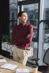 Smiling african american businessman standing near coffee to go and notebook in office.