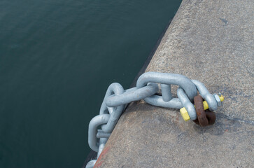 New metal chain attached with a shackle toold rusty ring in the port close