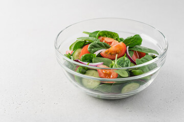 Fresh salad in  glass transparent bowl on white background. Spinach, tomato, cucumber, onion fresh vegetables for vegan, healthy diet
