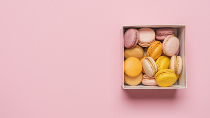 Macaroons almond biscuits in  gift box on pink pastel background. Traditional french gourmet pastries top view, copy space