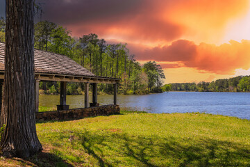 A brown wooden boat house on a gorgeous vast blue lakes surrounded by lush green trees, grass and...