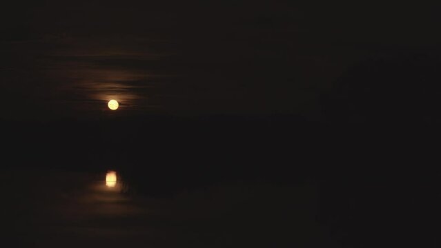 Timelapse of the rising moon over a night lake.