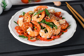 Salad with shrimps, arugula, cherry tomatoes, sweet peppers and sesame seeds on a white plate