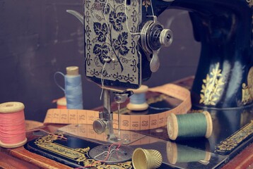 Close-up of the needle of a vintage sewing machine and sewing accessories: threads, tailor tape. Concept: sewing at home, business idea of additional income,fashion history.