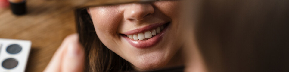 Young smiling woman looking at mirror while doing makeup indoors