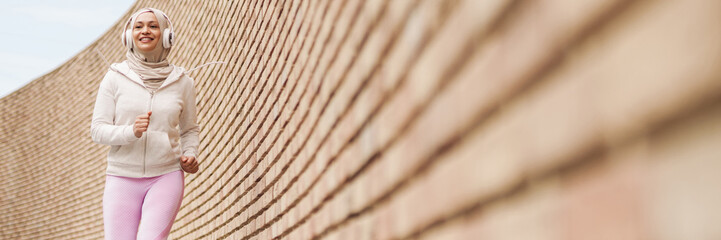 Middle eastern woman in hijab listening music with headphones and running