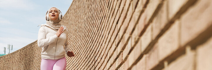 Middle eastern woman in hijab listening music with headphones and running