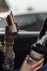 a girl driving her car snacks on fast food, coffee and french fries.