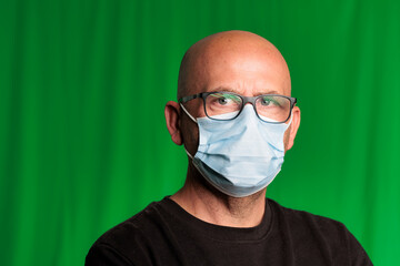 portrait bald man with glasses and green background with covid mask