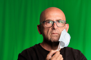 portrait bald man with glasses and green background with covid mask