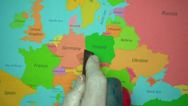 A hand painted in the color of the Russian flag cuts the map of Europe with a blade