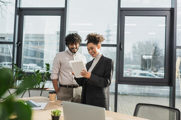 Smiling african american businesswoman holding digital tablet near indian colleague in office.