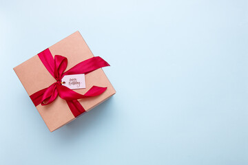 gift box with a satin ribbon and the inscription happy birthday on a light blue background with copy space