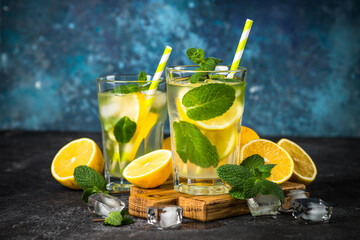 Fototapeta premium Lemonad in the glass. Traditional summer drink with lemon, mint and ice cube at dark table.