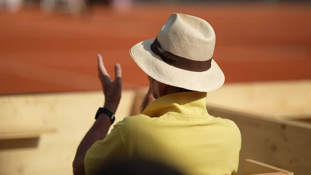 Spectator watching tennis match game clapping hands cheering from stadium seat wearing panama hat