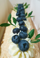 Meringue roll with a gentle airy cream, green leaves and blueberries