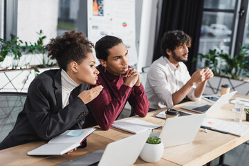 African american business people talking near laptops and blurred indian colleague in office.