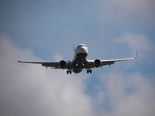 Commercial plane about to land at Barcelona airport on a sunny day with clouds in the background.