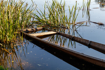 Fototapeta premium defektes Fischerboot am Flussufer mit Wasserspiegelung