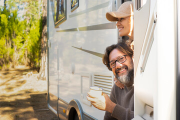 Mature man and woman outside the door of a modern camper van motor home parked in the forest....