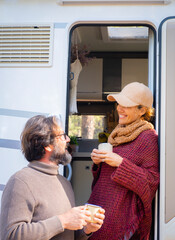 Adult couple talking happy outside the door of a camper van. Travel vacation and freedom with motor...