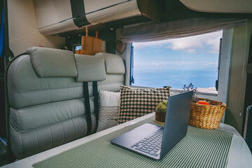 Interior of modern camper van motor home with table and sea ocean view. Laptop computer and...