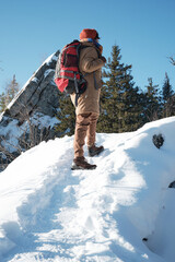 Vertical low angle shot of young man wearing warm clothes and backpack hiking to mountain top