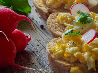 Scrambled eggs with herbs, radish and coriander on crispy wheat-rye bread, homemade breakfast