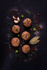 Raw meatballs, with micro greenery, with spices , on a black background , top view, homemade, no people,